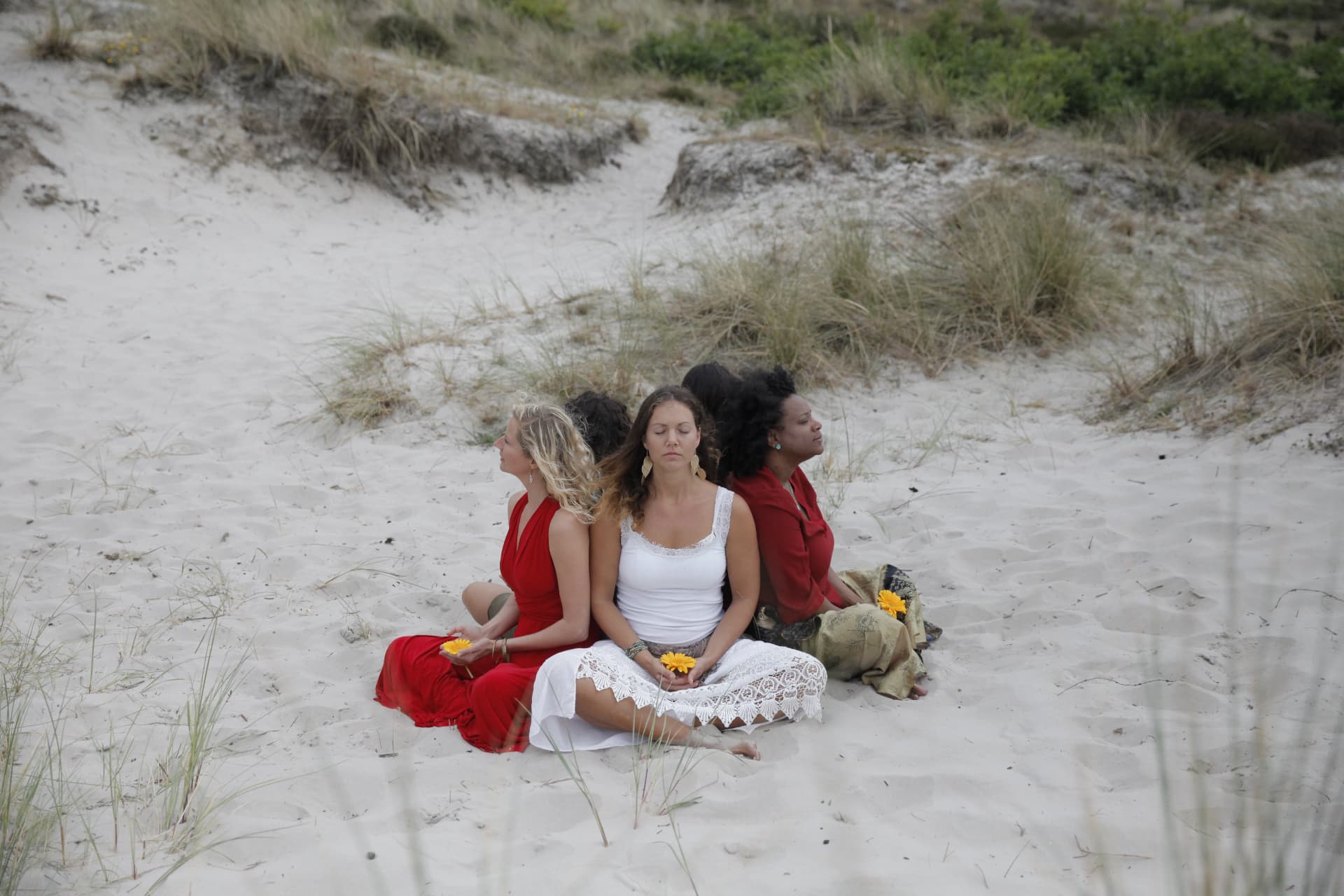Three women sitting back to back with yellow flowers in the dunes